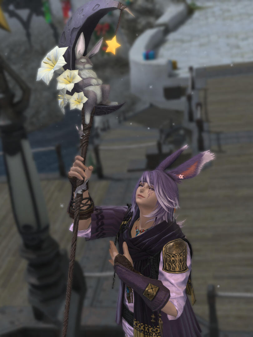 A male viera with purple hair and long ears posing cutely for the camera, holding up a white mage cane that has a crescent moon with a sleeping rabbit on it. He is wearing a pink shirt, purple bracers, and a purple scarf.